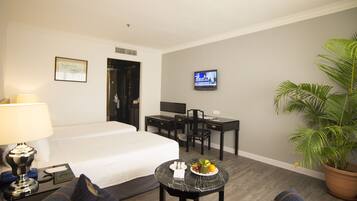 A hotel room with a bed, desk, chair, TV, and a potted plant.