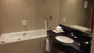 A modern bathroom with a bathtub, a sink, and a large mirror. There are toiletries on the sink counter and a towel hanging on the wall.