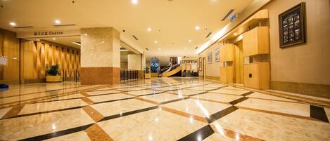 A spacious lobby with a geometric marble floor, a staircase, and a reception area labeled "M.I.C.E. Centre".