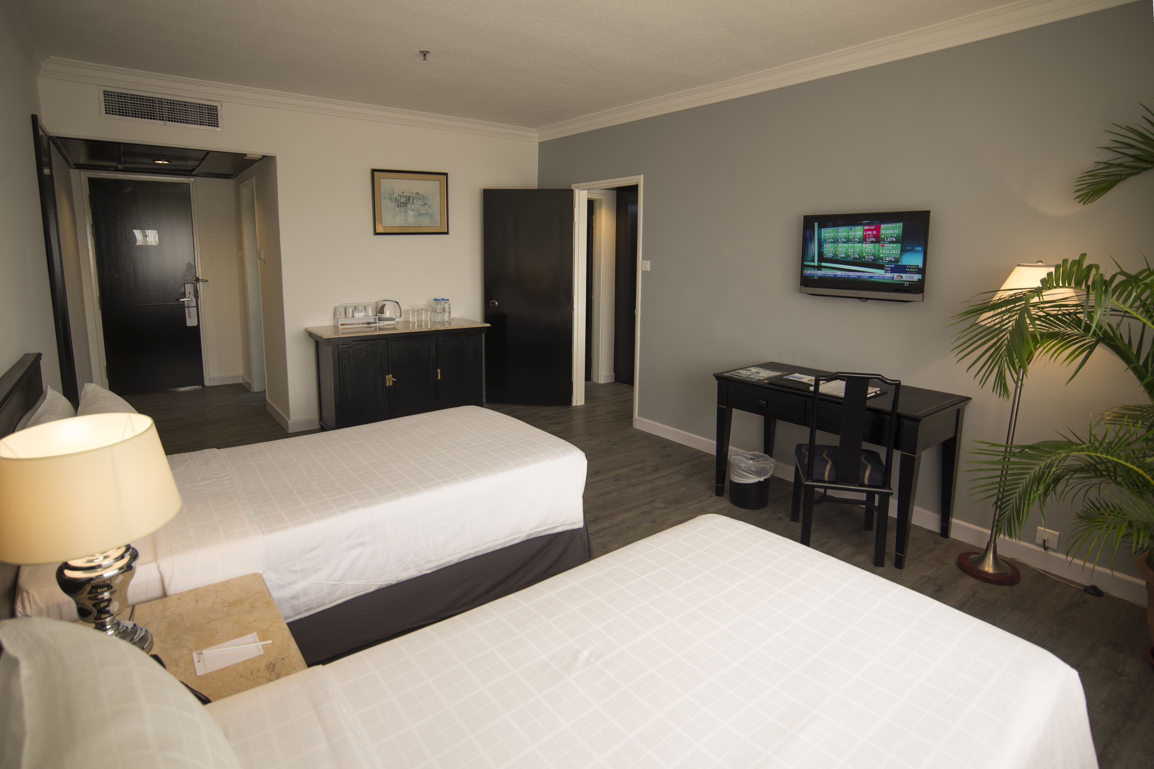 Una habitación de hotel con dos camas, un escritorio, un televisor y una planta.