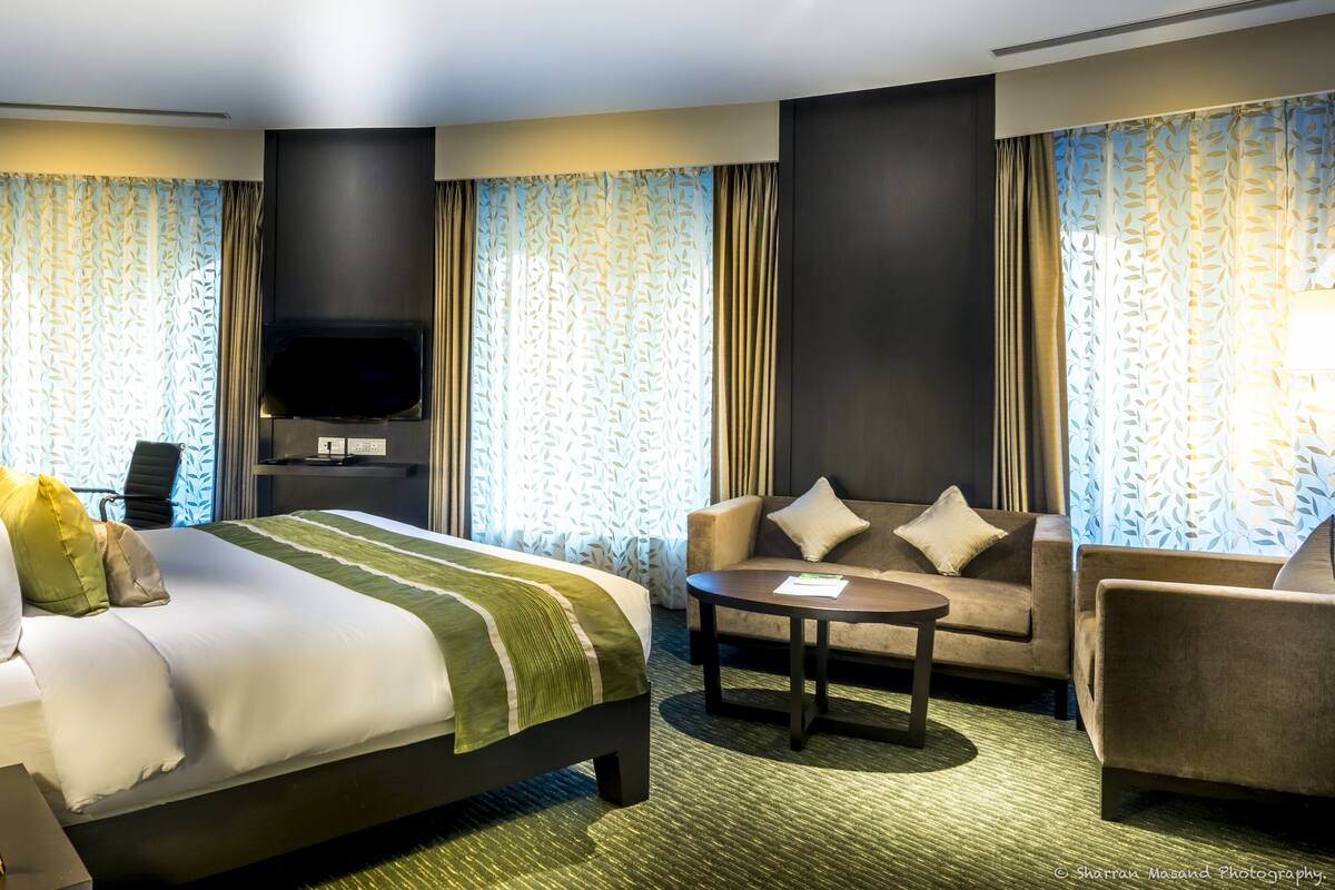 A hotel room with a large bed, a sofa, a coffee table, and a TV.