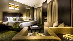 Habitación de hotel con cama, dos sillones, una mesita, un escritorio con silla, televisor y cortinas.