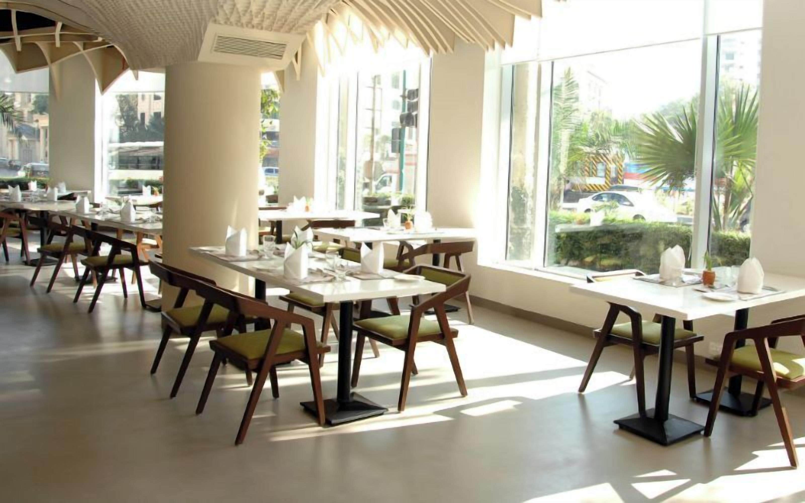 A spacious indoor dining area with multiple tables and chairs, large windows offering views of the outdoors, and a modern architectural design.