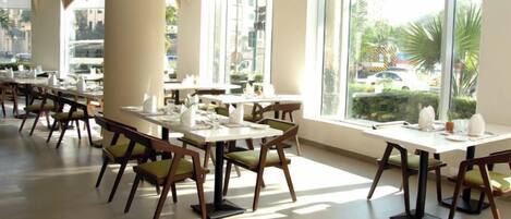 A spacious indoor dining area with multiple tables and chairs, large windows offering views of the outdoors, and a modern architectural design.