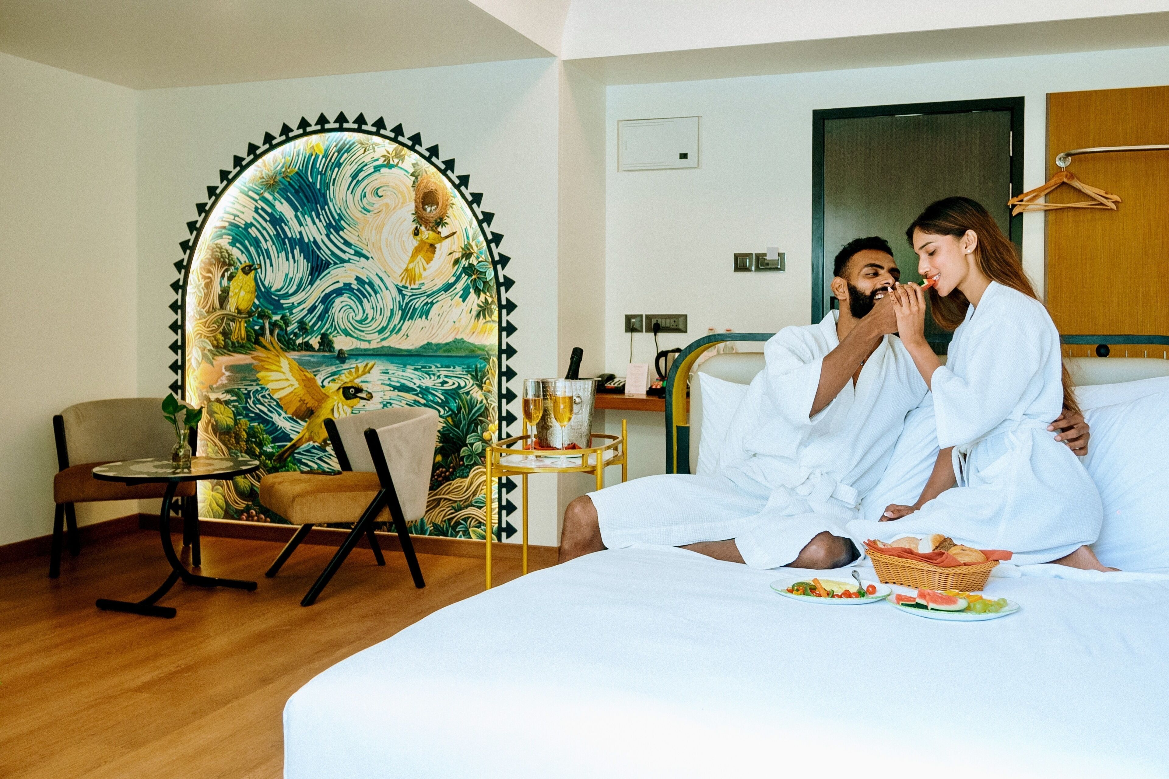 Een hotelkamer met een bed, een tafeltje met een mand brood, een stoel en een wanddecoratie.