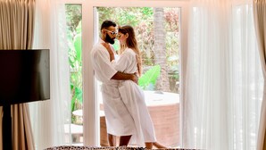 A couple embracing in a room with a large window, a flat-screen TV, and a bed with a patterned bedspread. - The Orchid Passaros Goa - Adults Only Resort (Benaulim)