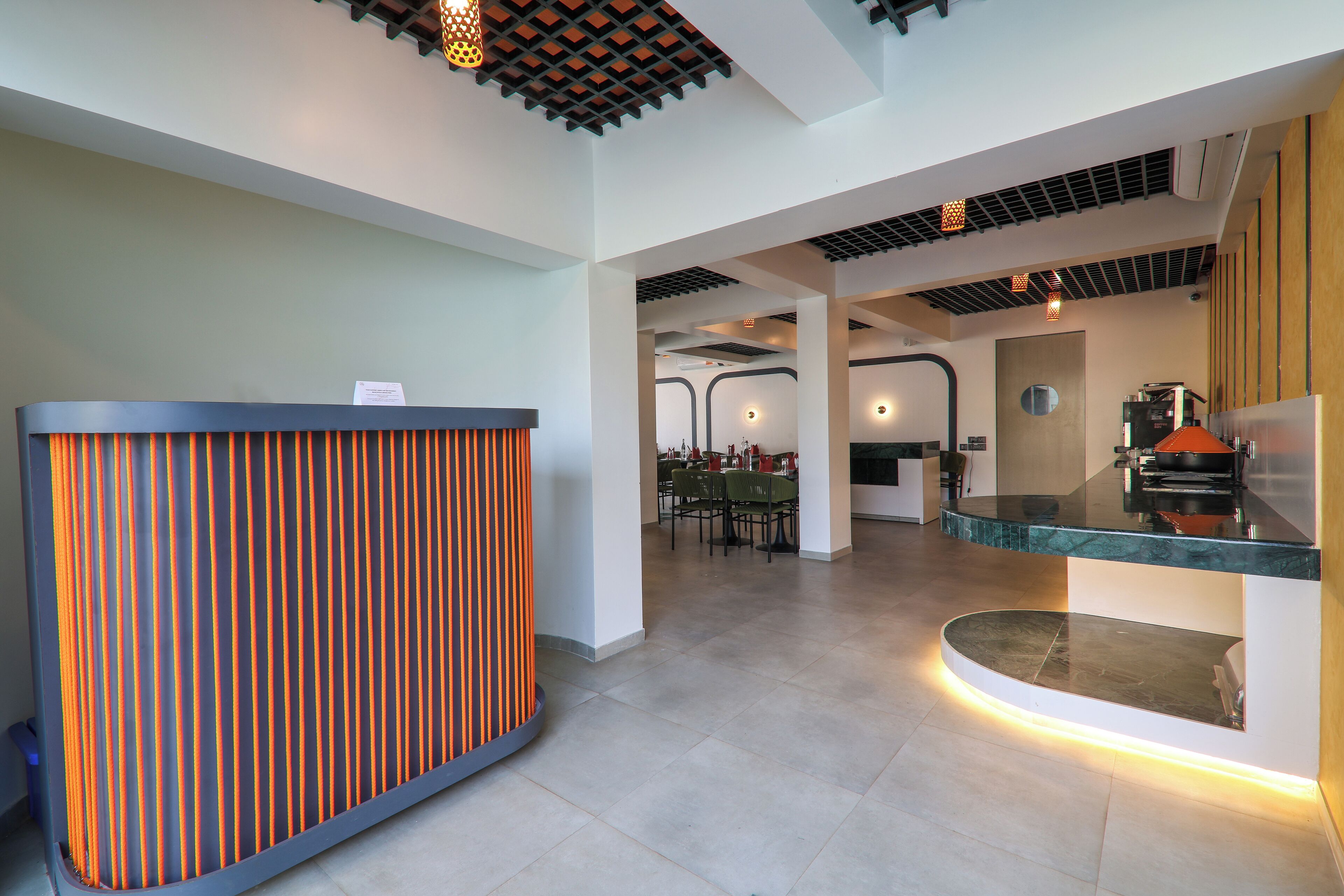 A modern reception area with a striped counter, a seating area with tables and chairs, and a kitchen area with a stove and refrigerator.