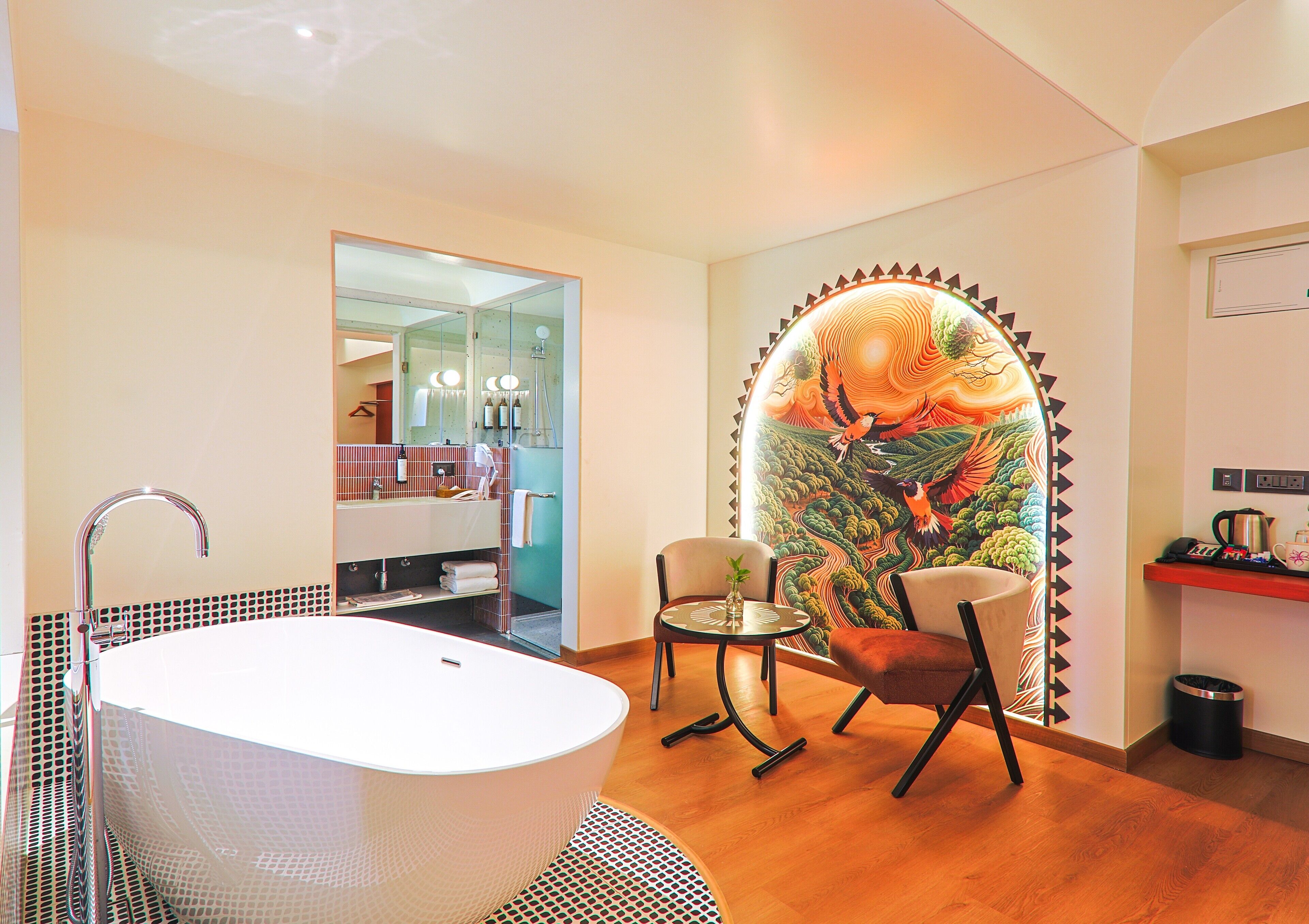 A modern bathroom with a freestanding bathtub, two chairs, a small table, and a large mural on the wall.