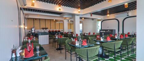 A restaurant with green chairs and tables, a kitchen in the background, and a patterned floor.