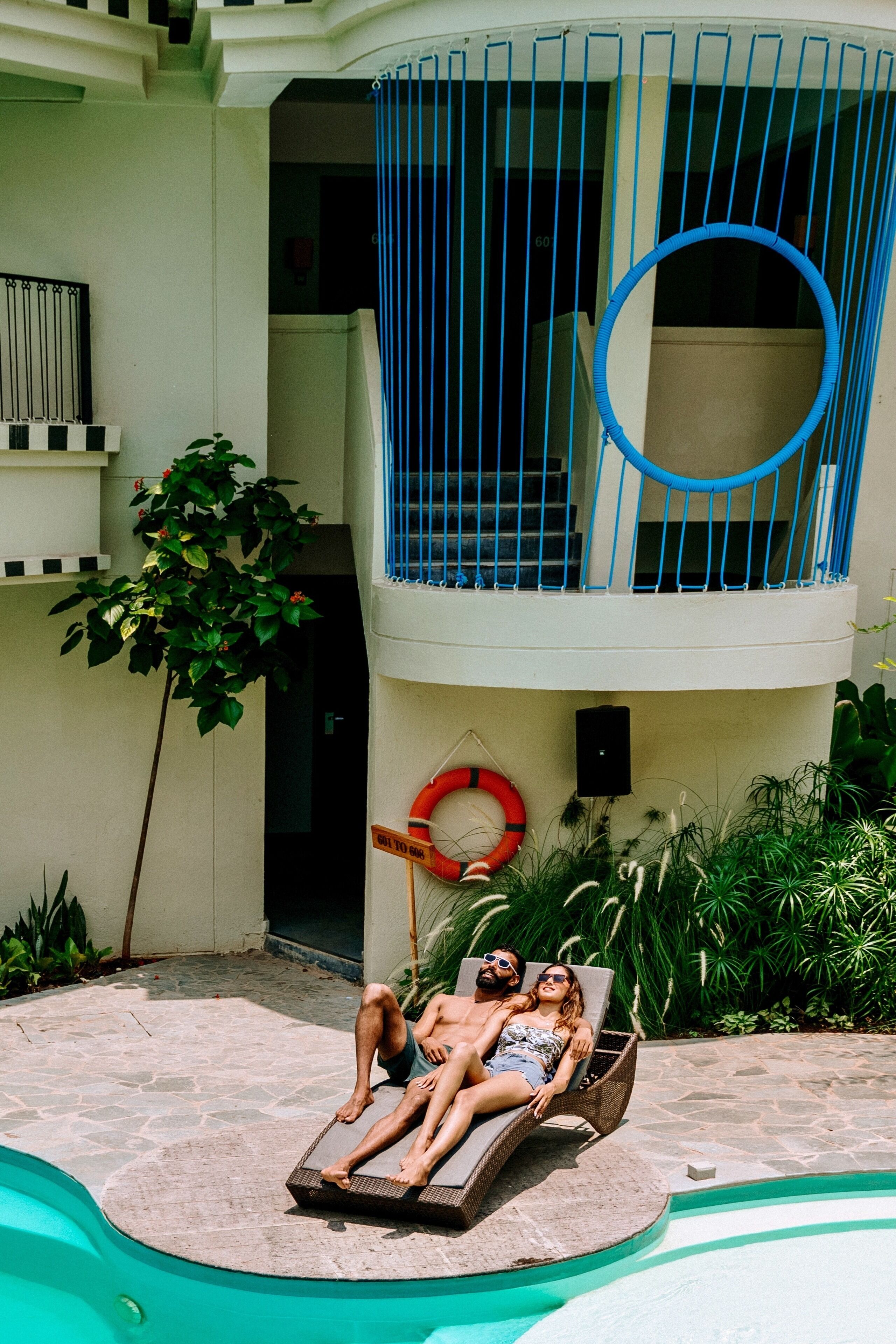 A pool area with a lounge chair, a lifebuoy, and a blue circular object on the balcony.