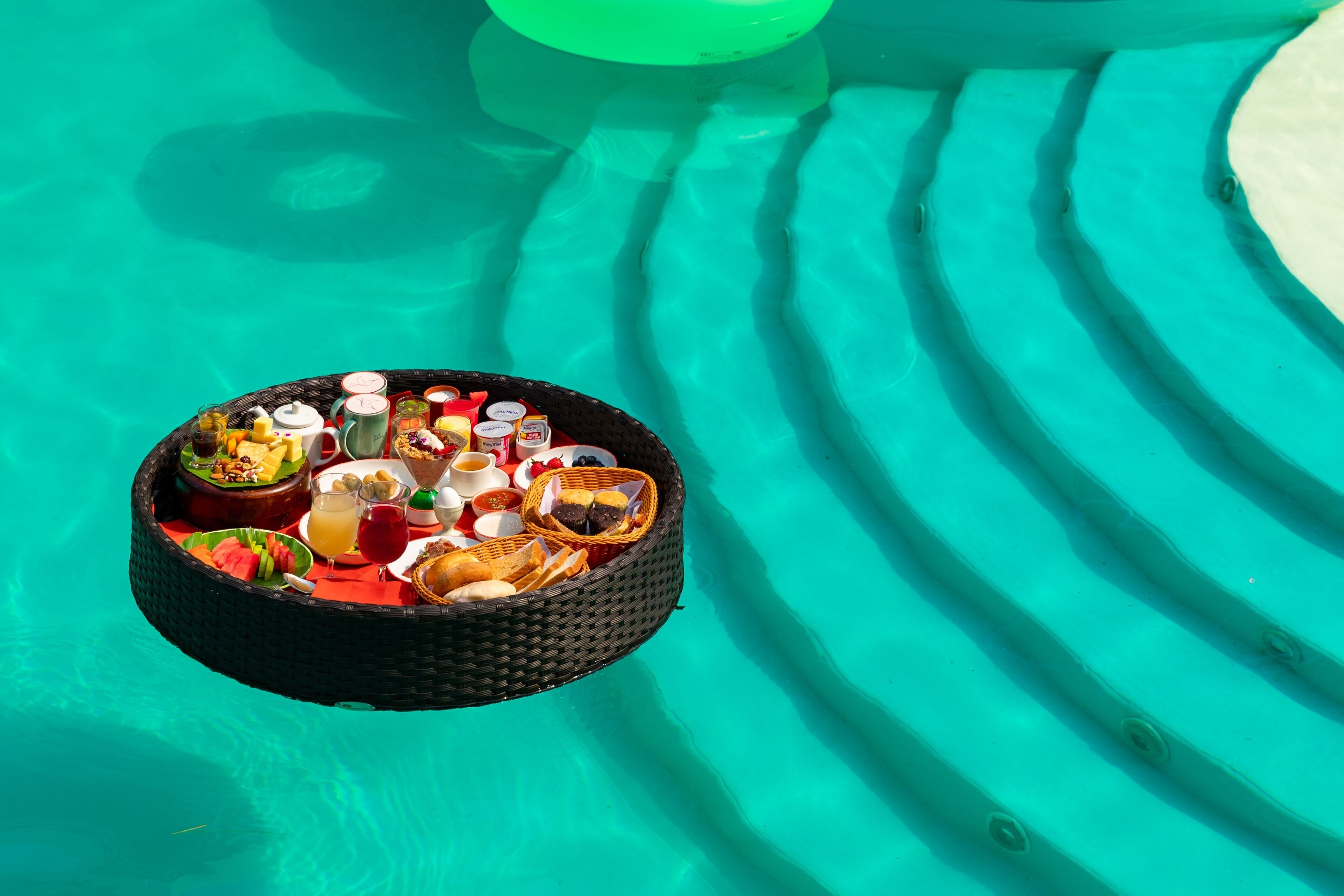 A floating tray with various food items and drinks over a pool.