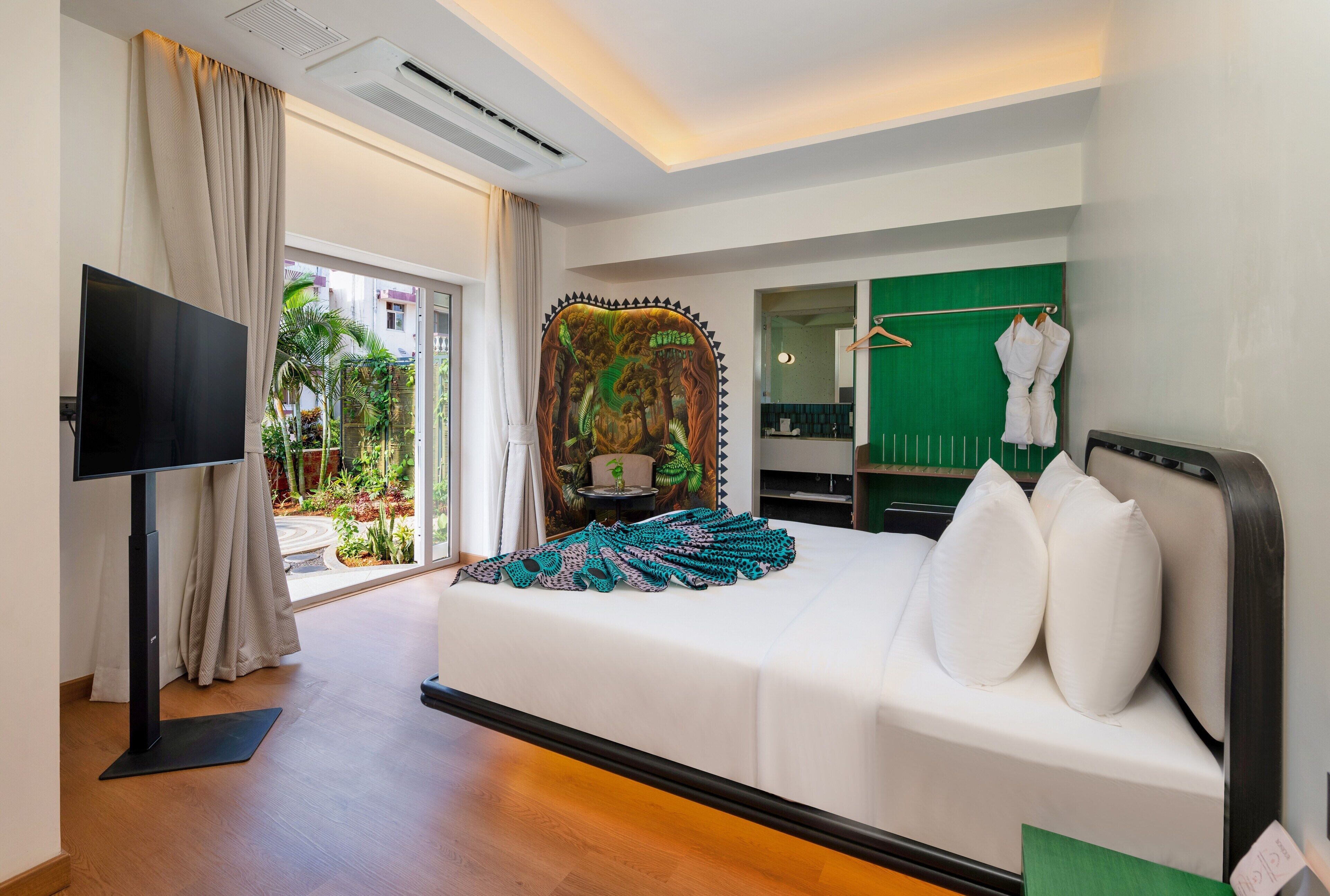 A hotel room with a bed, a TV, a green wall, and a view of the outdoors.
