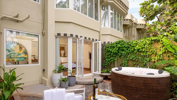 A spa area with a hot tub, a table with wine glasses, and a view of the interior through glass doors. - The Orchid Passaros Goa - Adults Only Resort (Benaulim)