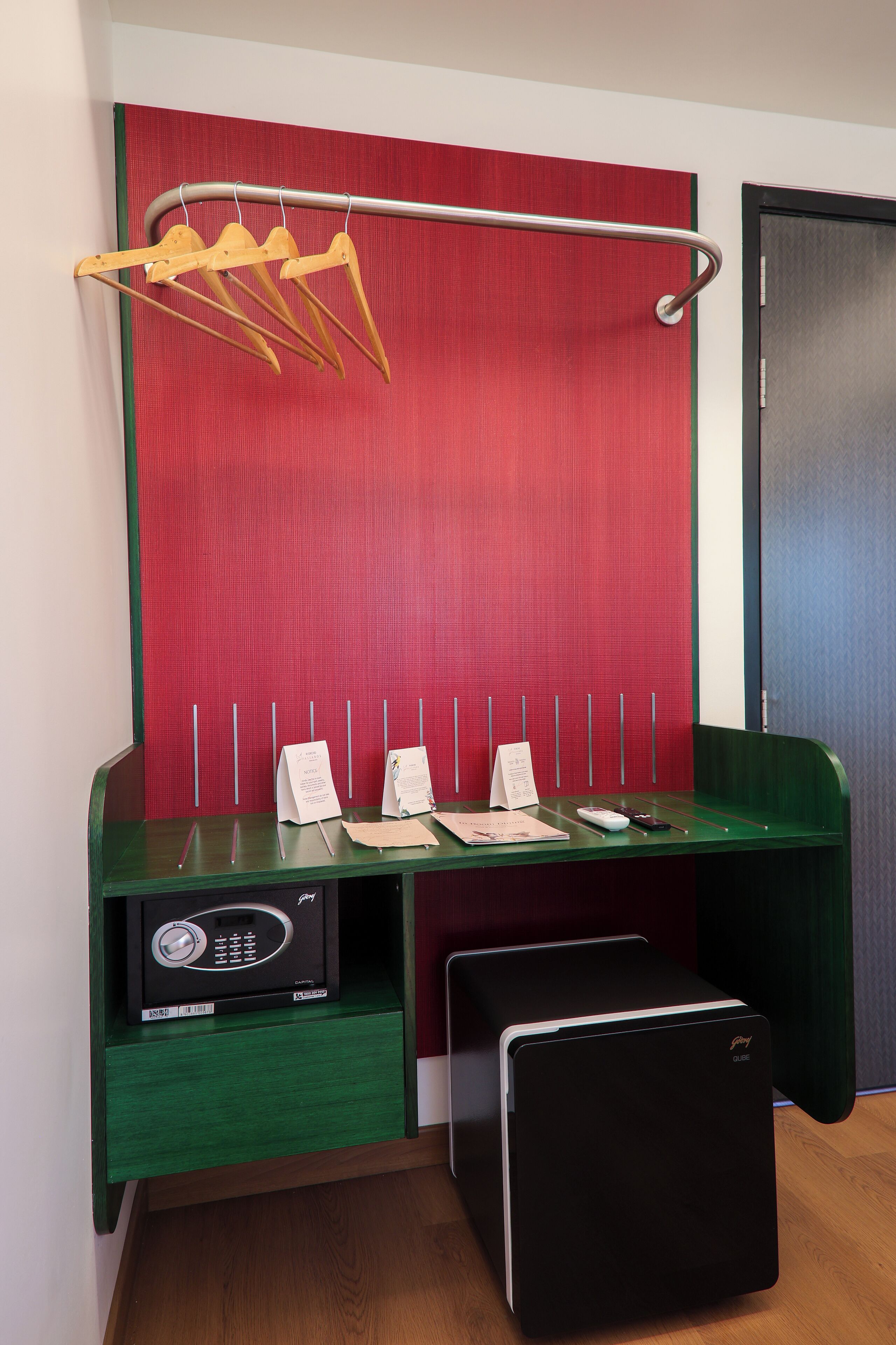 A room with a green desk, a red partition, a metal rack with hangers, a black safe, and a green bench.