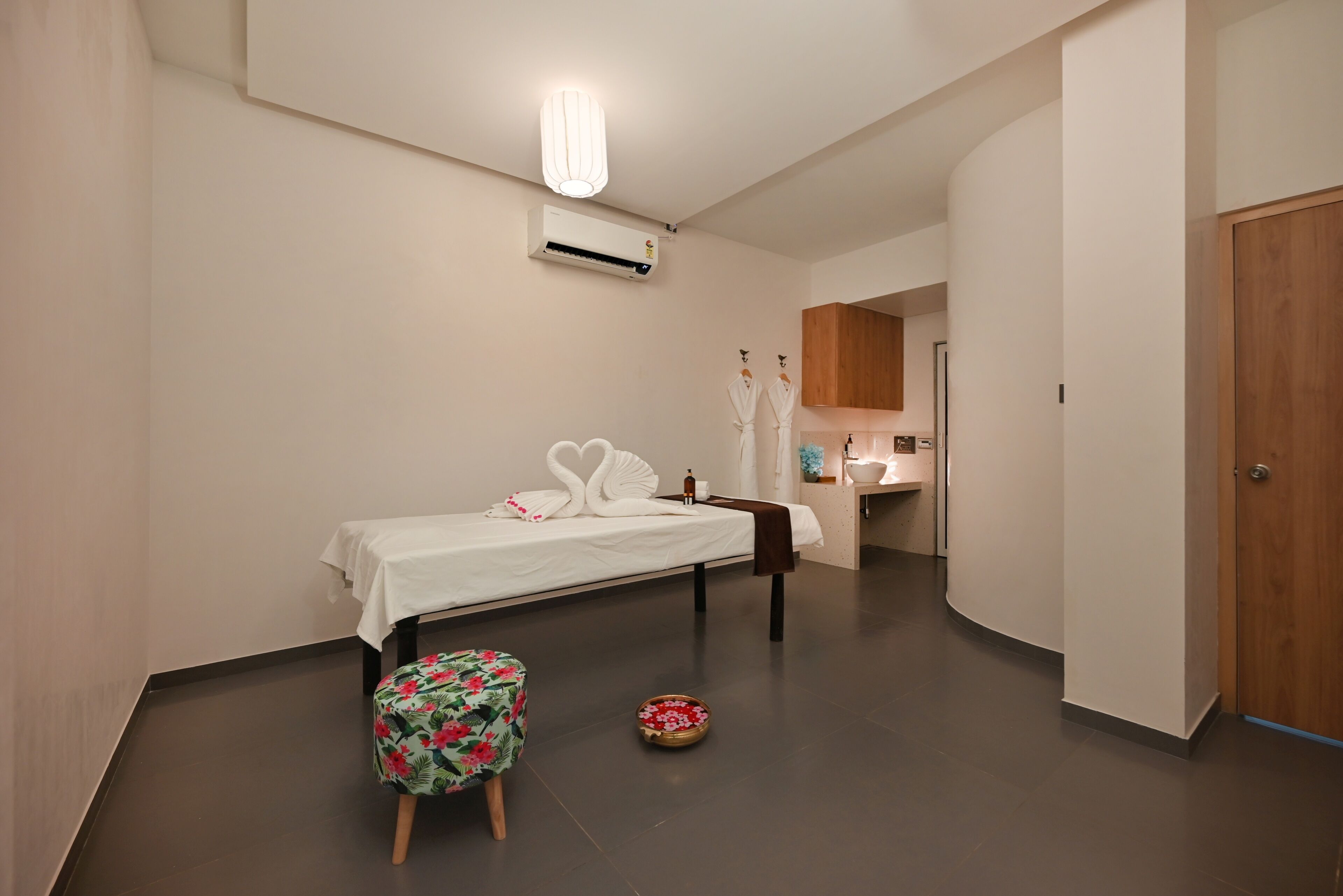 Un dormitorio moderno con una cama, un taburete pequeño y una mesa redonda con un objeto decorativo.