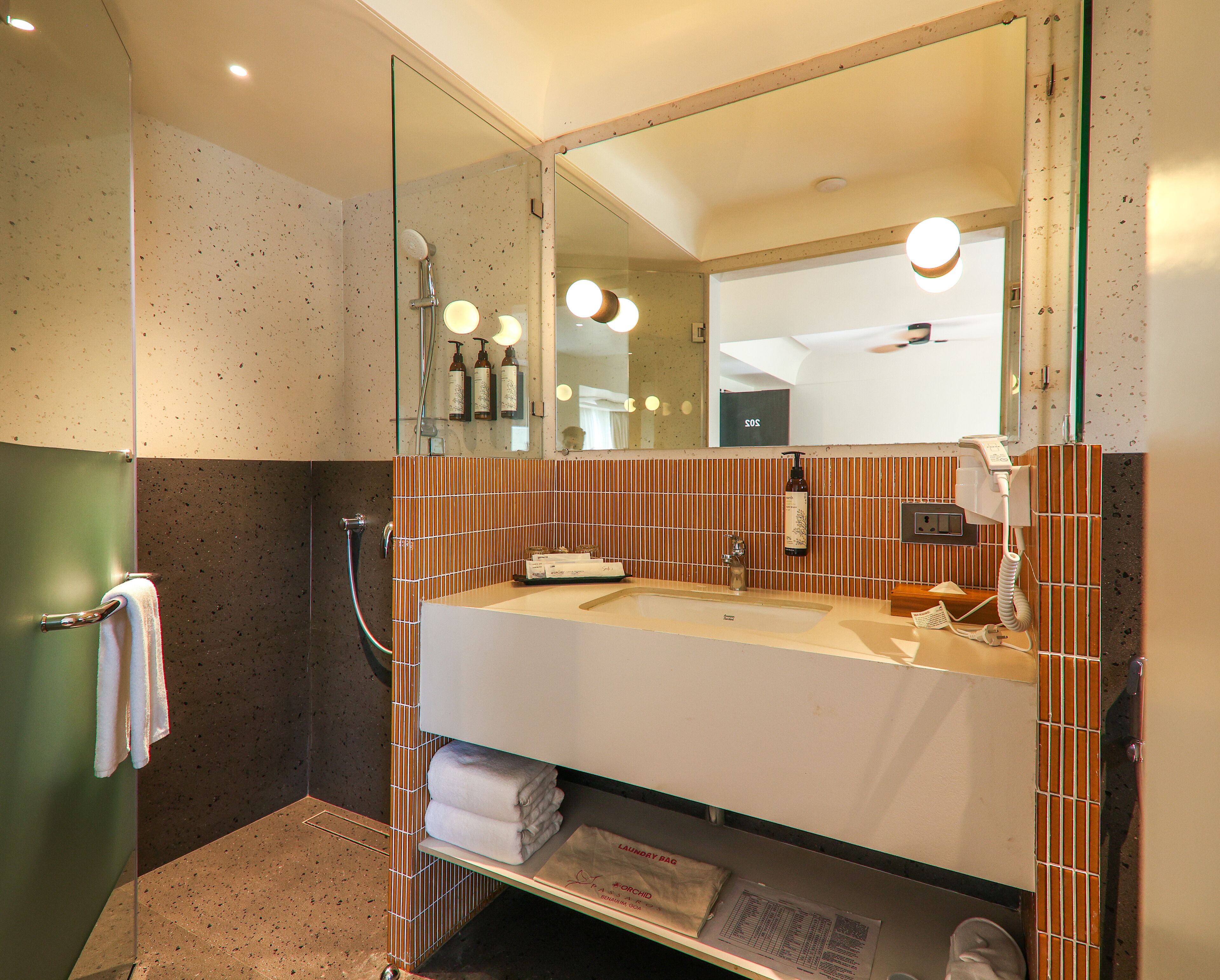 Un baño moderno con cabina de ducha de vidrio, un espejo grande y un lavabo con artículos de tocador.