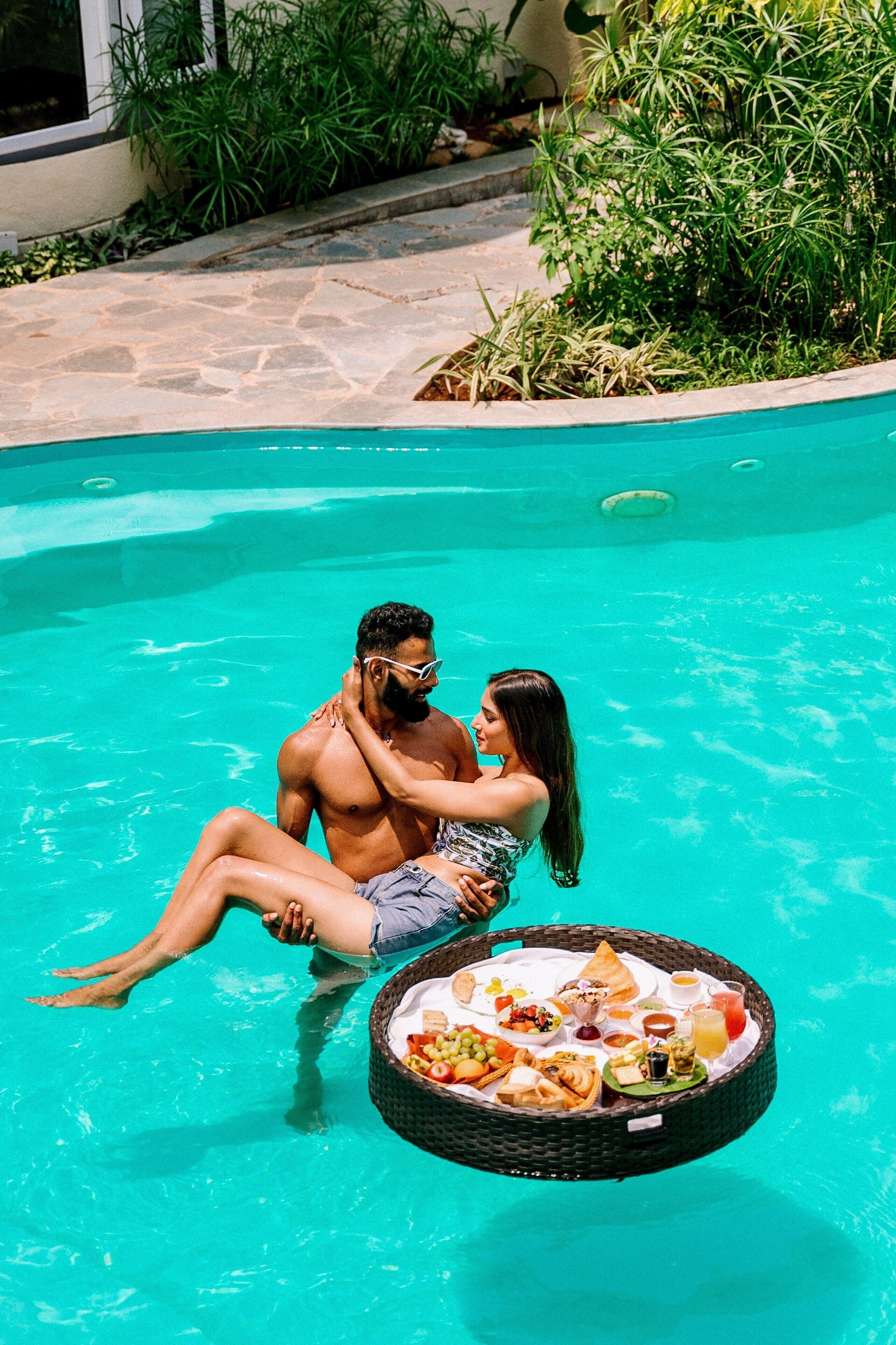 A couple sitting in a pool with a floating tray of food.