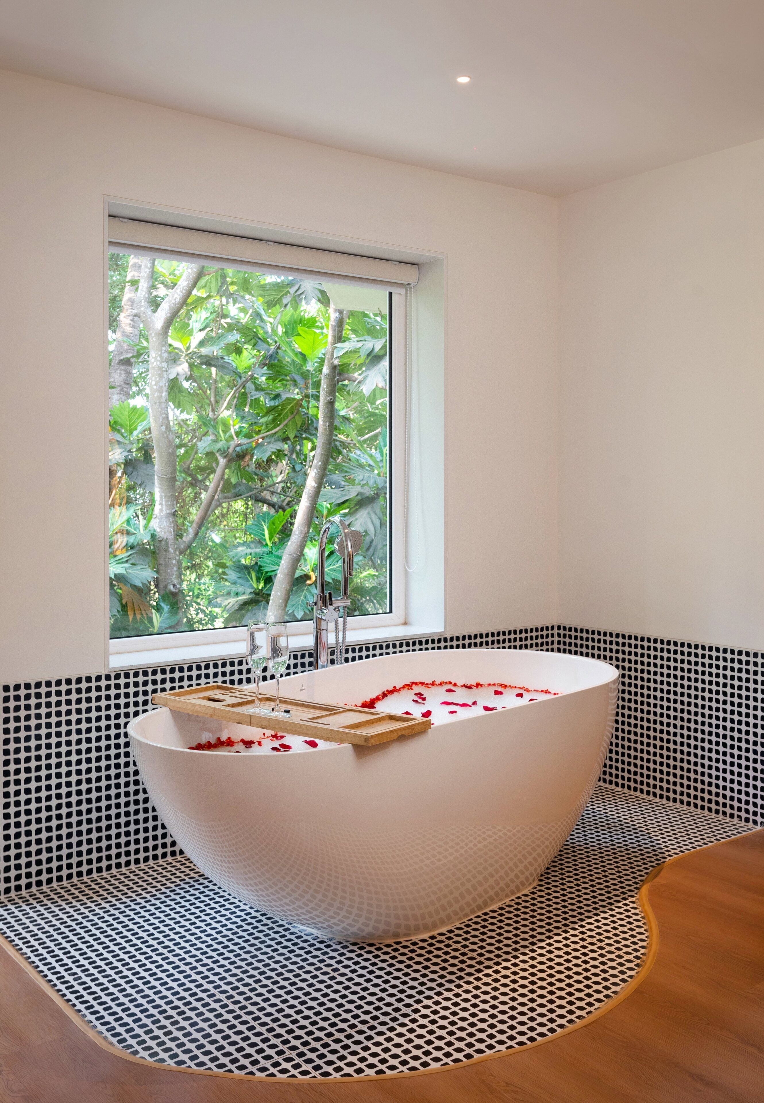 Un baño moderno con una bañera independiente, un ventanal con vistas a la vegetación y un suelo con estampado blanco y negro.