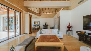 A spacious living room with a large wooden table, white sofas, and a television on a black cabinet.