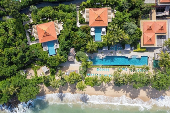 Vista aérea de um resort com vários edifícios, uma piscina central e uma praia.
