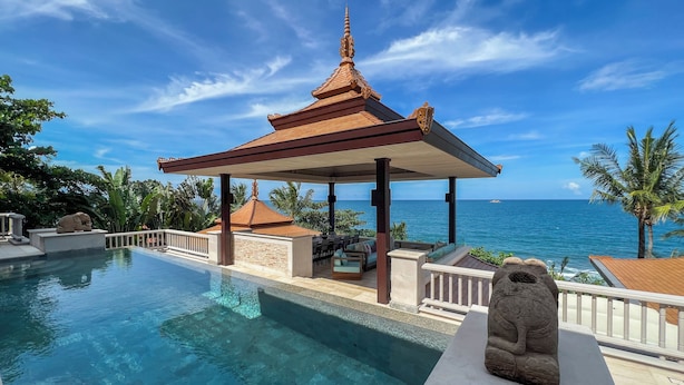 A poolside area with a traditional pavilion, clear blue water, and a view of the ocean.