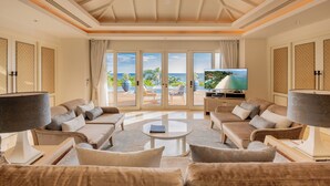 Amplia sala de estar con televisor grande, asientos cómodos y vista al océano a través de puertas correderas.