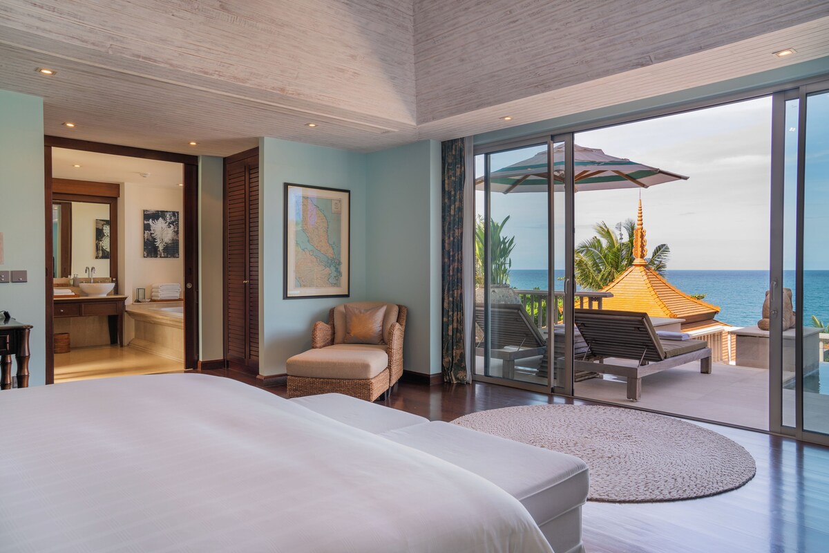 Un dormitorio amplio con una cama grande, una zona de estar con vista al océano y un baño con lavabo y espejo.