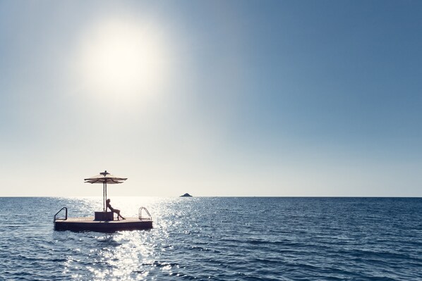 A person relaxing on a floating platform with an umbrella in a calm sea. - Trisara Villas & Residences Phuket (Choeng Thale)