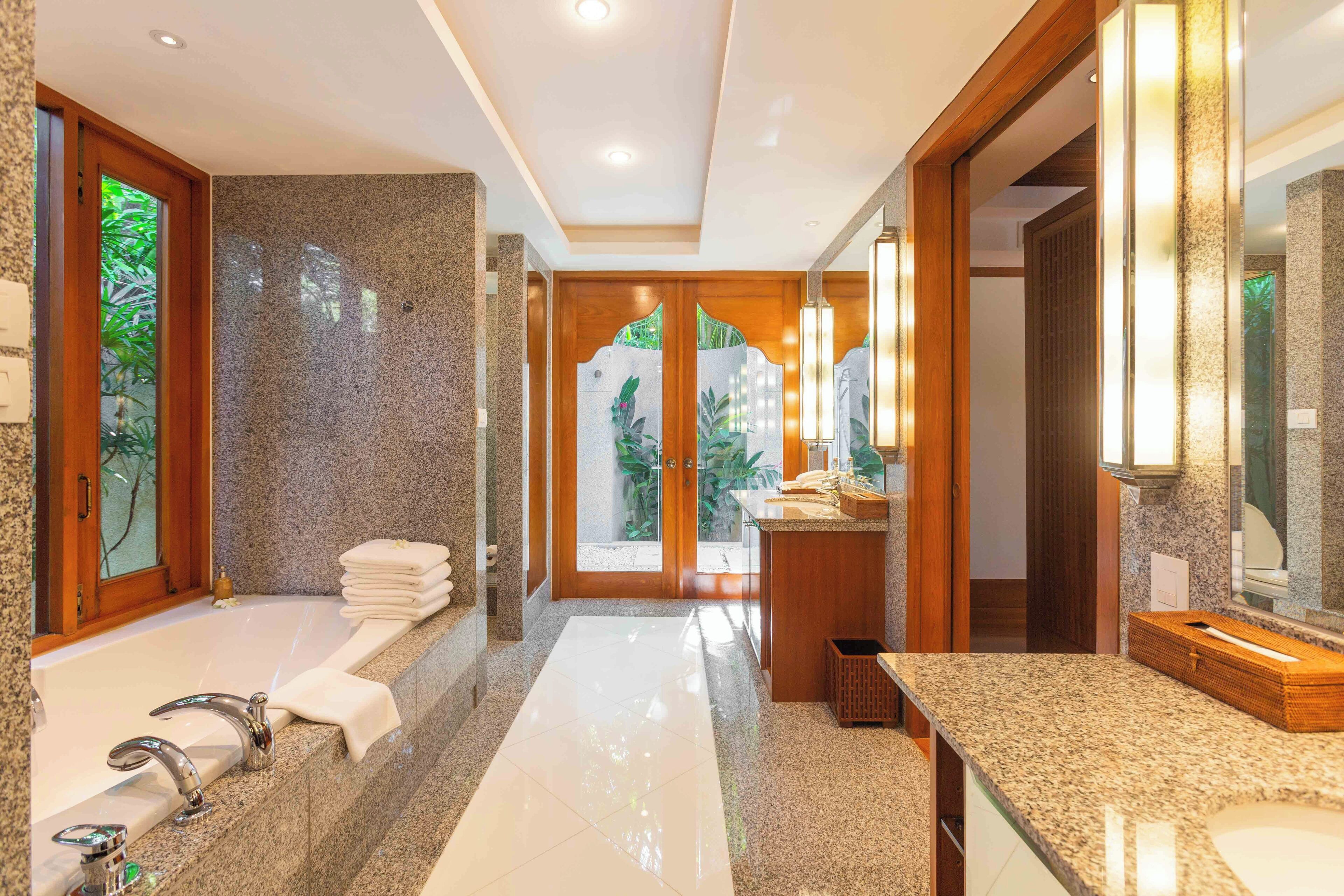 A modern bathroom with a large bathtub, a vanity with a mirror, and a view of greenery outside.