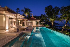A luxurious pool area with a clear view of the sea, a covered seating area, and a well-lit building. - Trisara Villas & Residences Phuket (Choeng Thale)