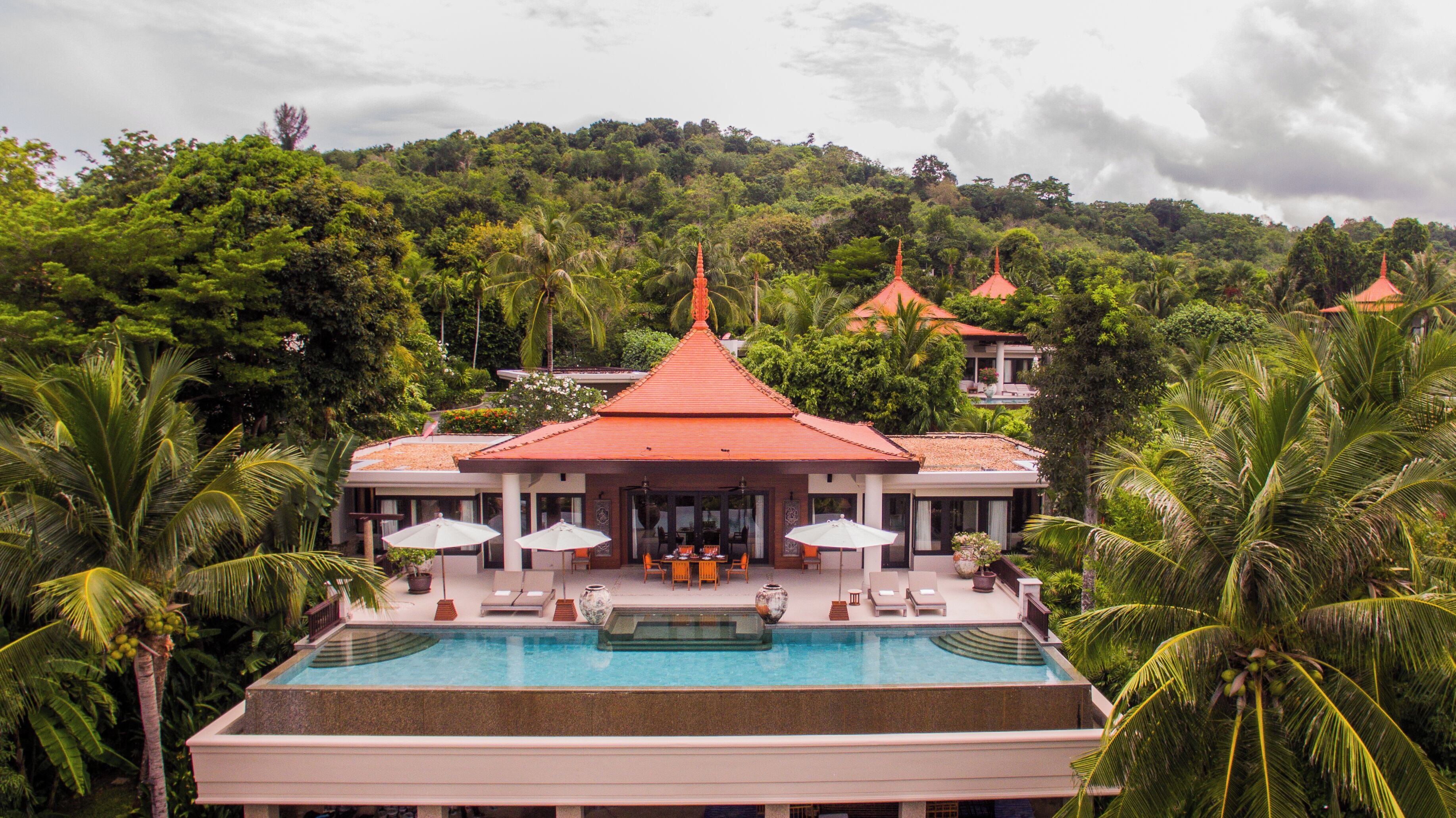 A resort with a swimming pool, a dining area, and a building with a red roof.