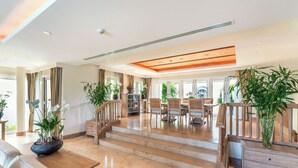 A spacious living area with a wooden staircase, a dining set, and potted plants.