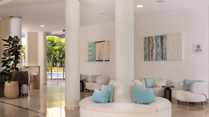 A modern lobby with a white sofa, teal cushions, and a large potted plant. - AluaSun Lago Rojo - Adults Recommended (Torremolinos)