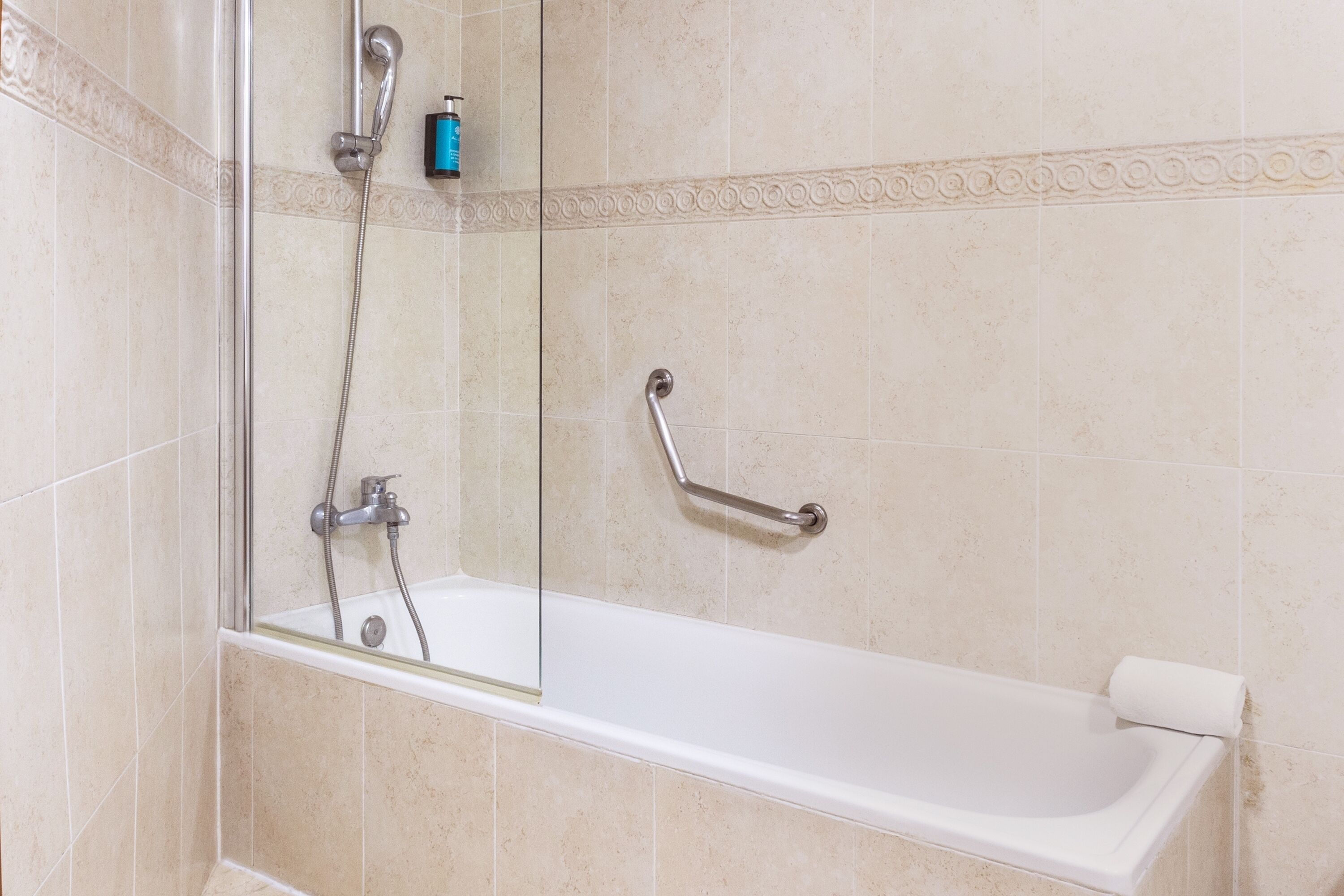 A bathroom with a glass-enclosed shower, a white bathtub, and a handrail.