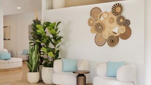 A modern living room with a white sofa, two blue cushions, a round wooden coffee table, and a wall-mounted woven art piece. - AluaSun Lago Rojo - Adults Recommended (Torremolinos)