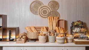 A buffet setup with various breads and pastries in woven baskets, a bottle of sauce, and a decorative wall piece. - AluaSun Lago Rojo - Adults Recommended (Torremolinos)