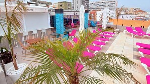 Una terraza en la azotea con una palmera, mobiliario exterior y vistas a la ciudad.