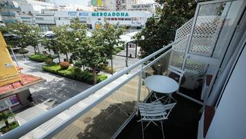 Een balkon met een witte tafel en stoelen, met uitzicht op een straat met een Mercadona supermarkt en andere gebouwen.
