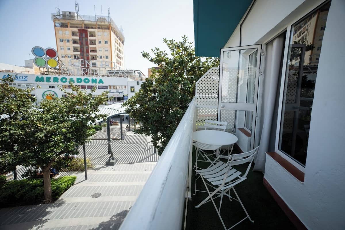 A balcony with a white table and chairs, a view of a plaza with a Mercado Azteca sign, and a building under construction in the background.