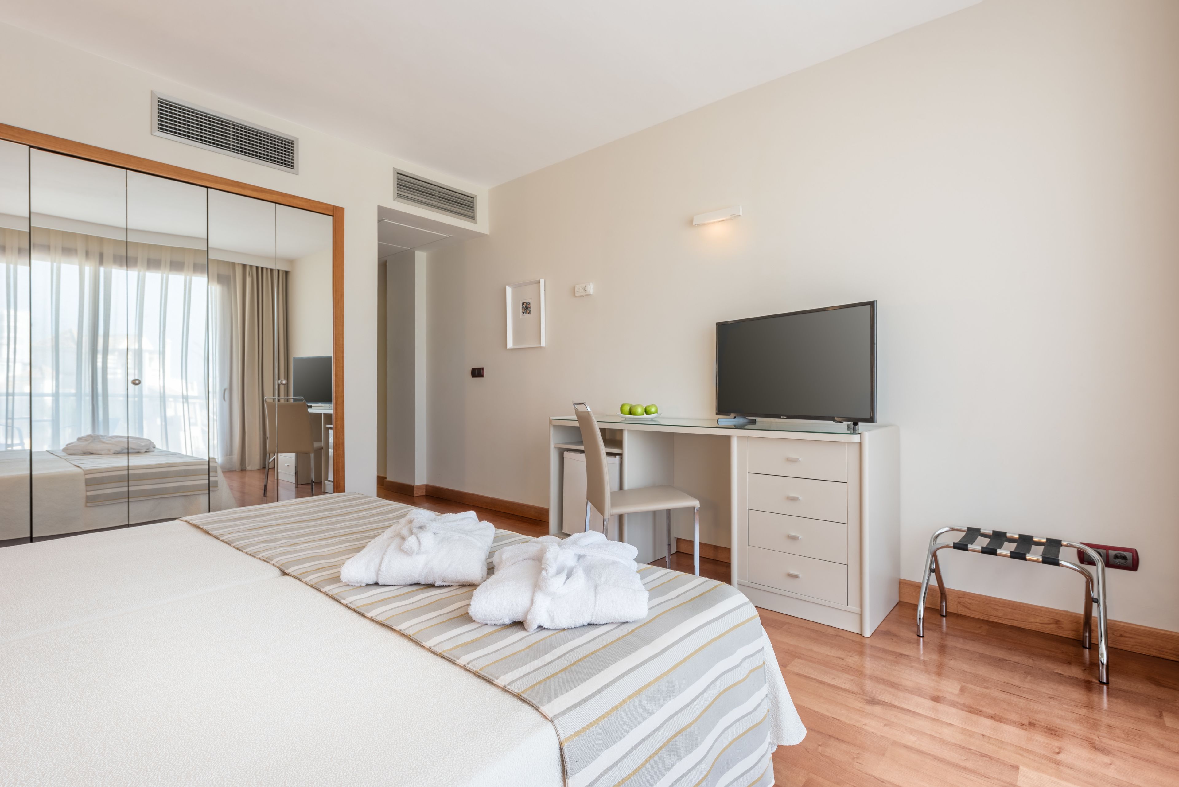 A hotel room with a bed, a desk, a television, and a small stool.