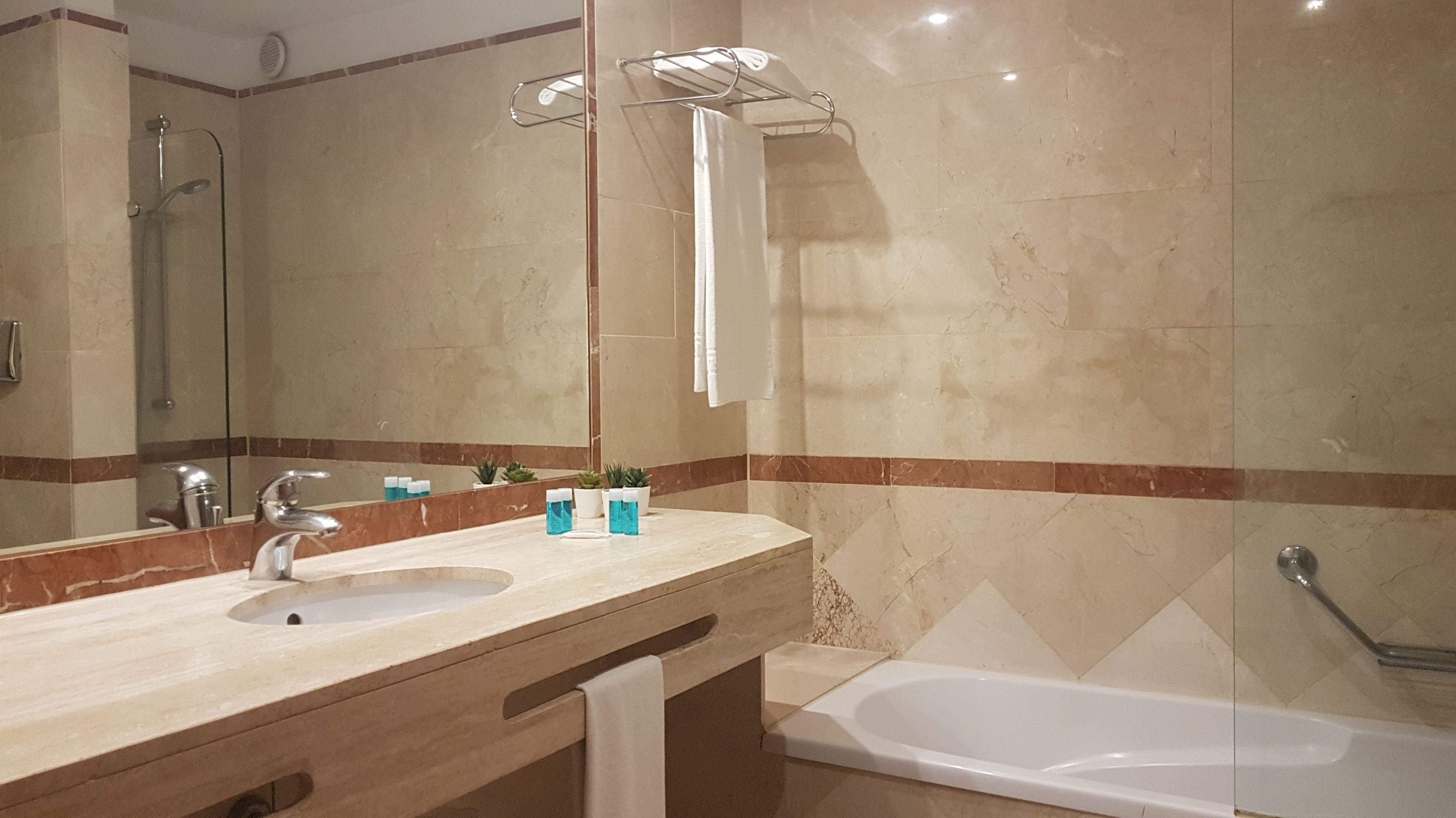Un baño con lavamanos, espejo, toallero, ducha y bañera.