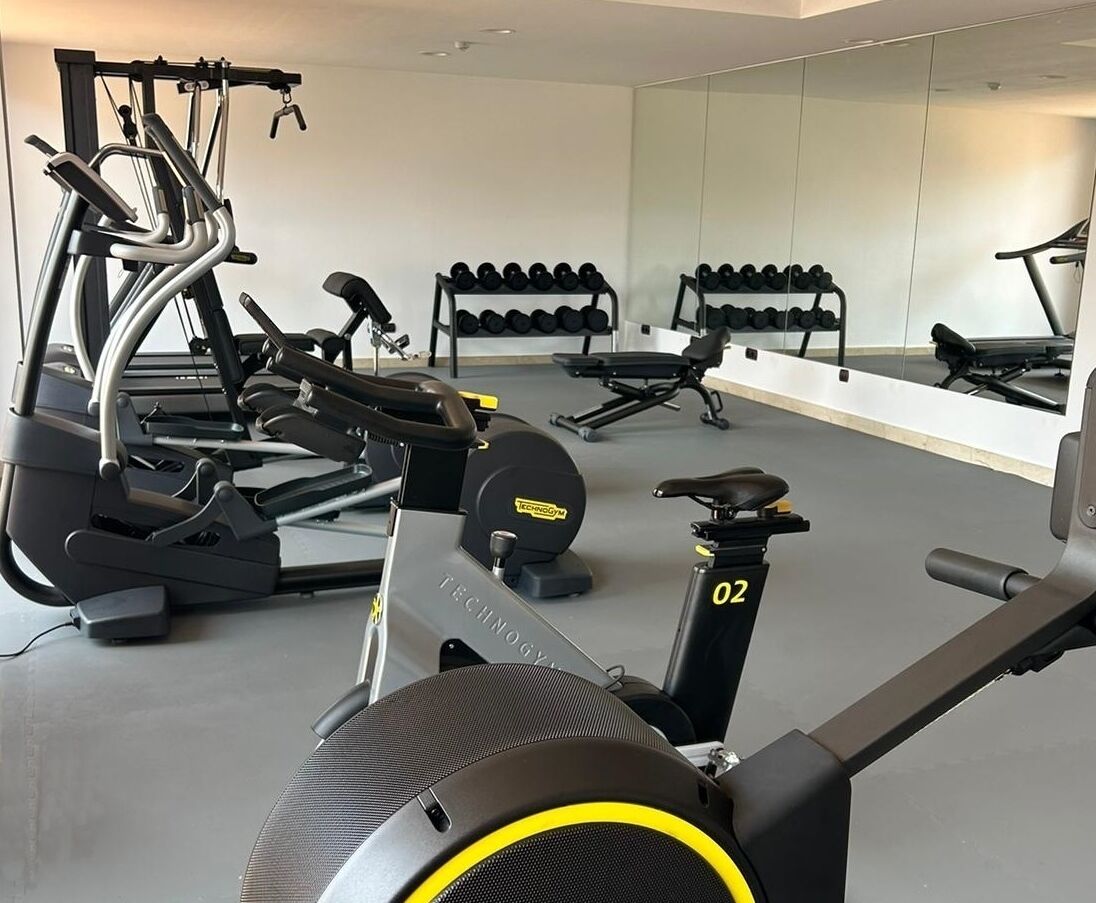 Una palestra con macchinari cardio, pesi e uno specchio lungo la parete.