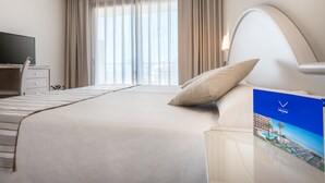 Habitación de hotel con una cama grande, un escritorio con televisor de pantalla plana, una ventana con cortinas y vistas a un paisaje urbano.