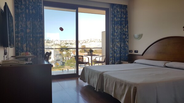 Habitación de hotel con cama, escritorio y balcón con vistas a la ciudad.