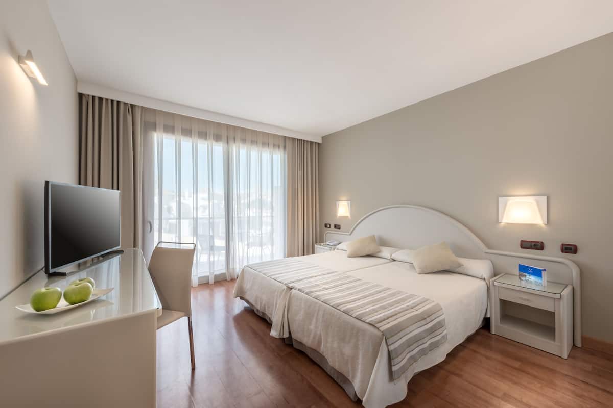 A hotel room with a bed, bedside tables, a TV, and a desk with apples.