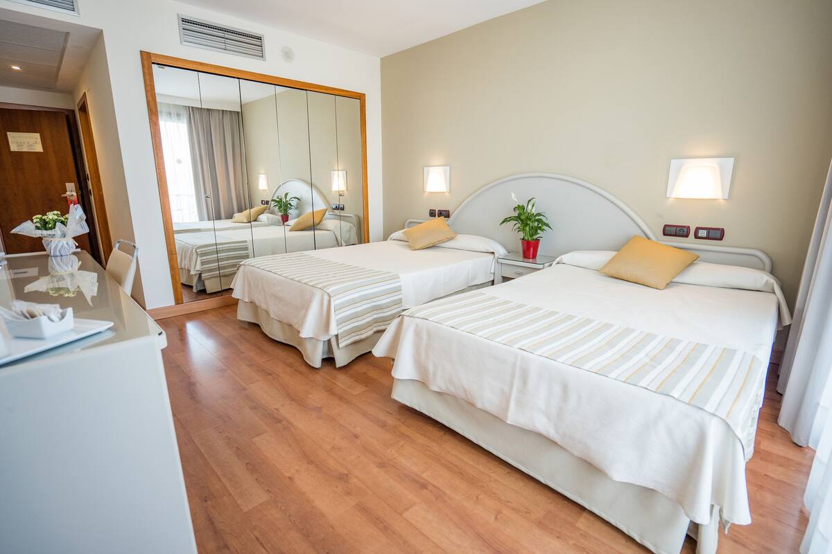A hotel room with two beds, a desk with a computer, and a large mirror.