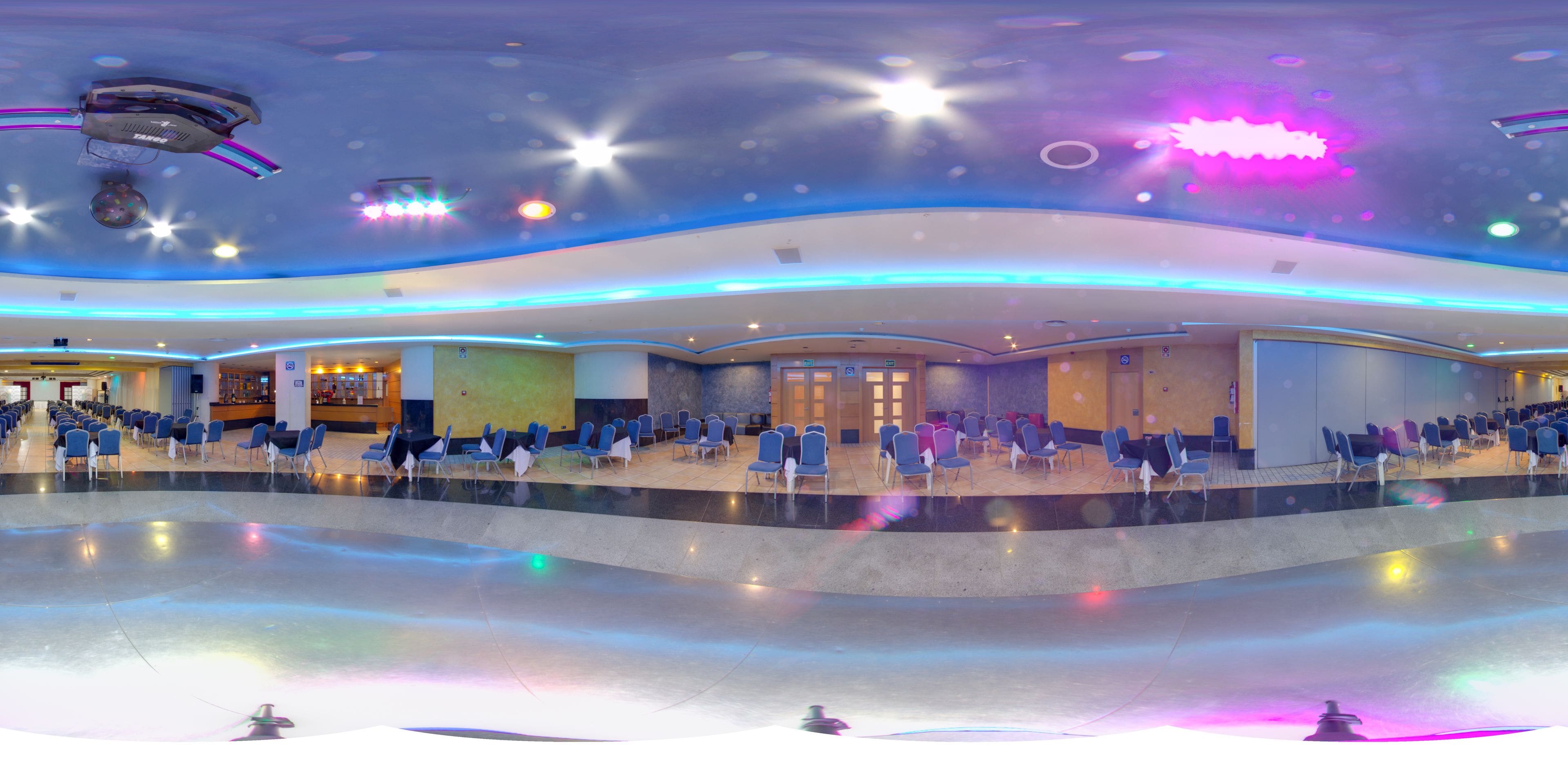 A spacious indoor area with rows of blue chairs, a stage, and a ceiling with star-like light fixtures.