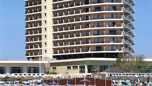 A multi-story hotel with balconies, a beach area with sun loungers, and a boat on the water. - Hotel Puente Real (Torremolinos)