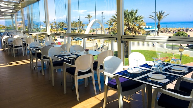 A restaurant with tables and chairs, large windows, and a view of the beach. - Hotel Puente Real (Torremolinos)