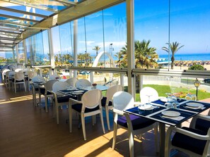 Un ristorante con tavoli e sedie, ampie finestre e vista sulla spiaggia.